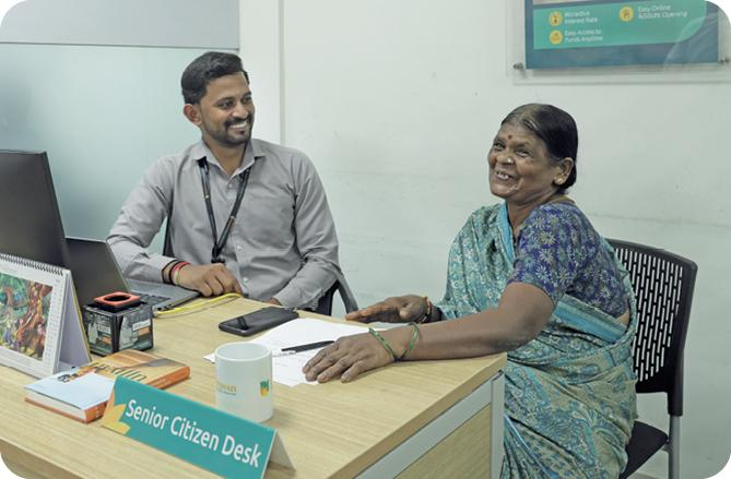 An elderly woman speaking with a staff member at a senior citizen desk.